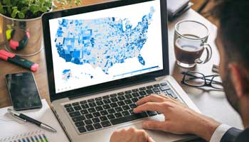 A man sitting at his laptop computer viewing a county data map of the U.S.A.